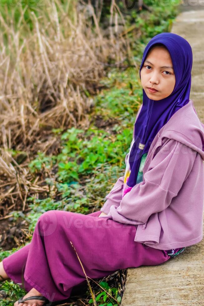 kant visie van een vrouw vervelend een hoofddoek zittend naast een rijst- veld- weg in de ochtend. foto