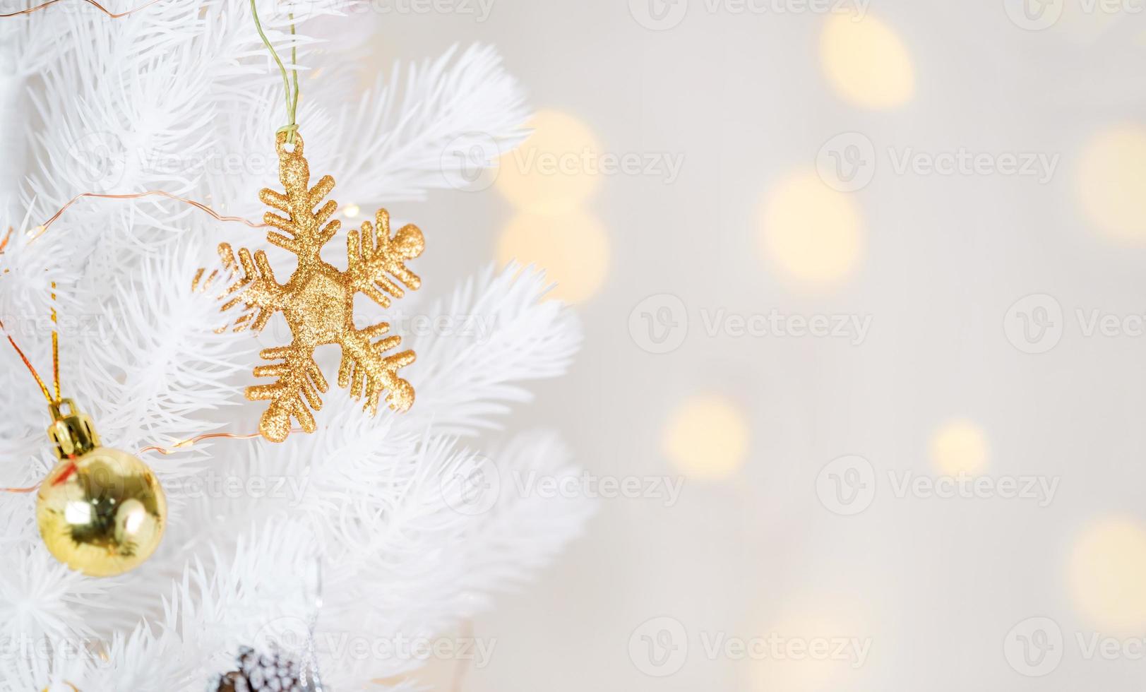 gouden sneeuwvlok en decorbal hangend aan witte kerstboom foto