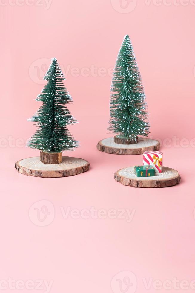 kerstboom op houtblok met huidige doos op pastelroze foto