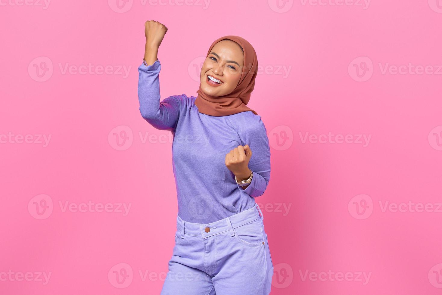 vrolijke jonge aziatische vrouw die de overwinning viert, euforisch over prestatie op roze achtergrond foto