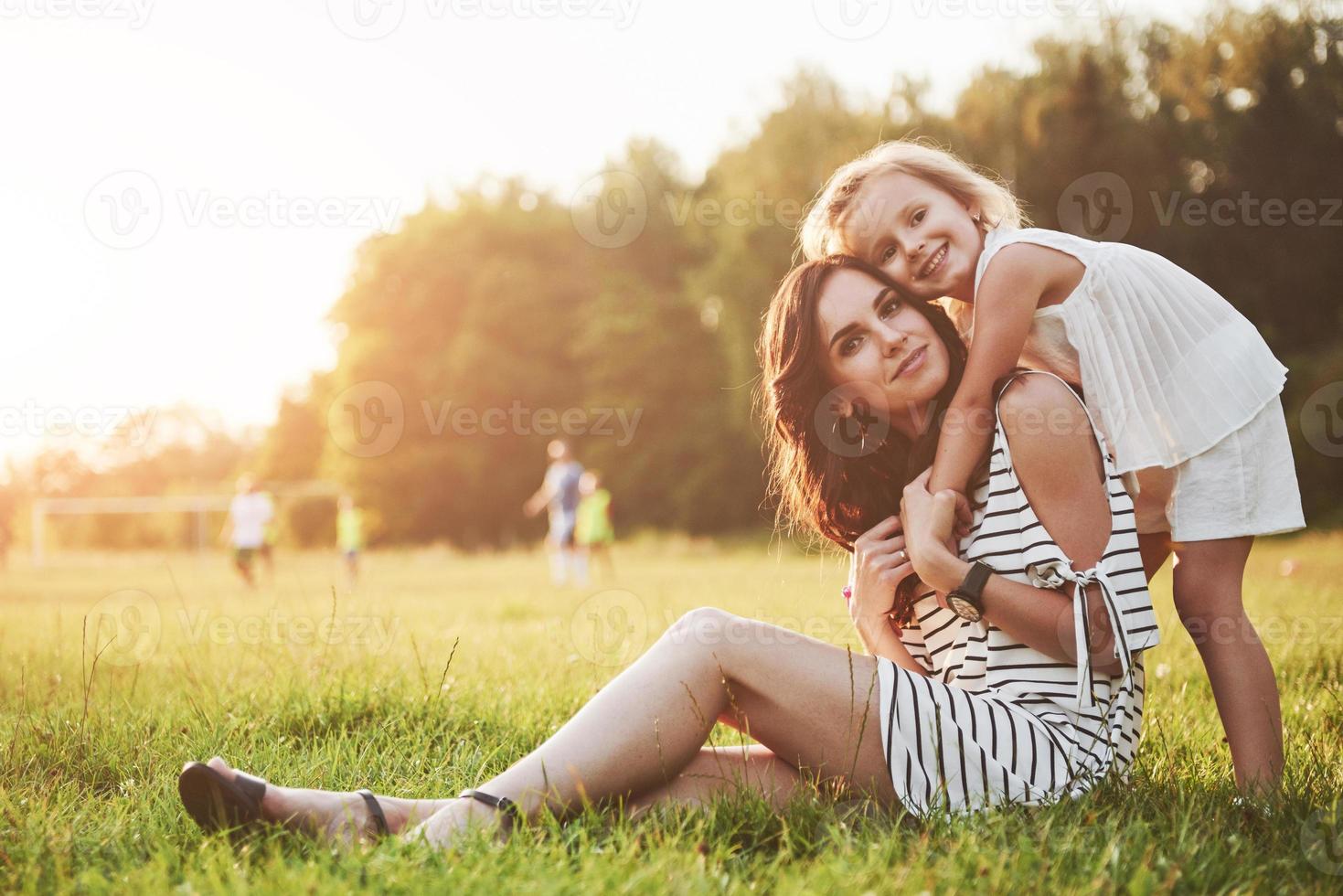 gelukkige moeder en dochter knuffelen in een park in de zon op een heldere zomerse achtergrond van kruiden. foto