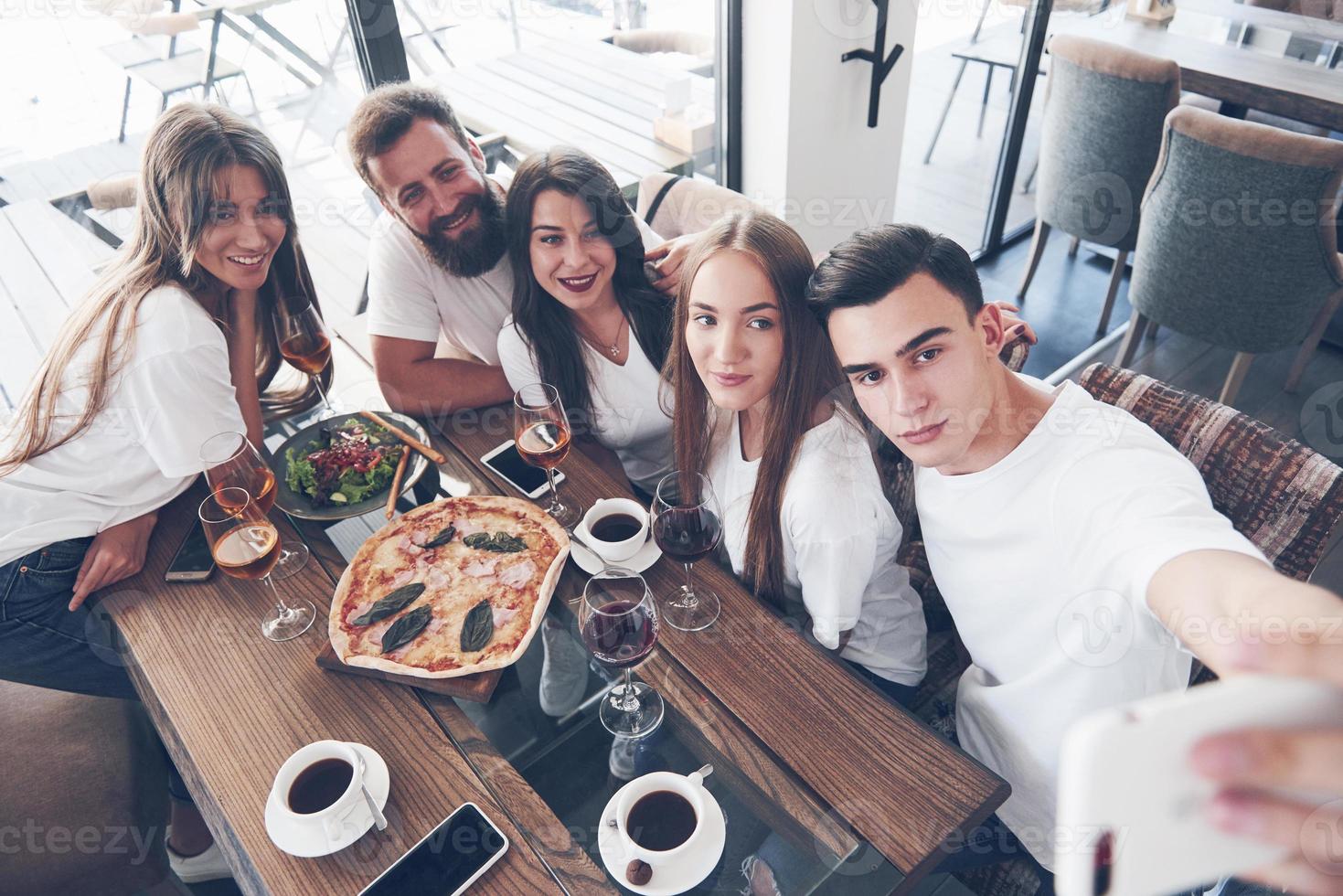 een groep mensen maakt een selfie-foto in een café. de beste vrienden verzamelden zich aan een eettafel, aten pizza en zongen verschillende drankjes foto
