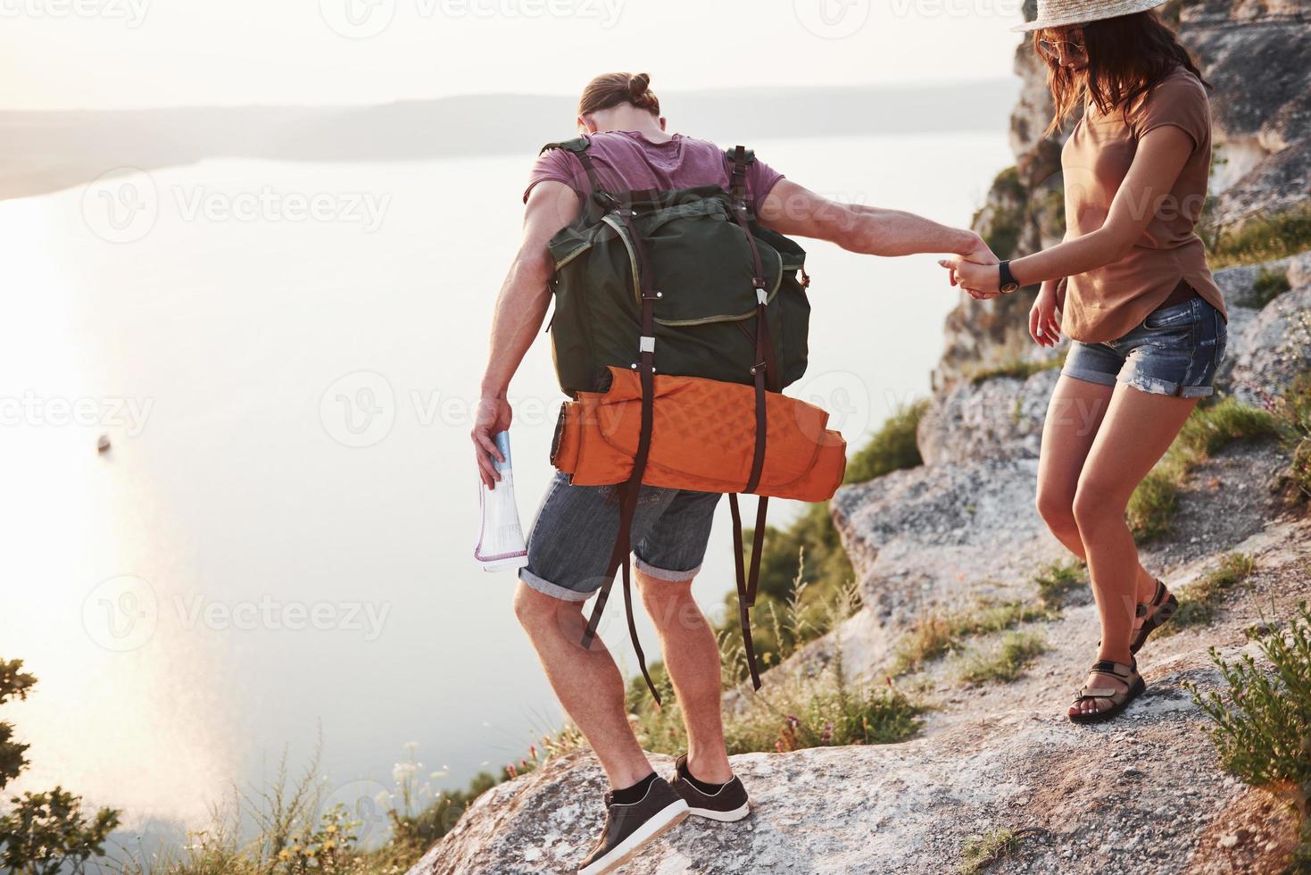 twee toeristische mannen en vrouwen met rugzakken klimmen naar de top van de berg en genieten van de zonsopgang. reizen levensstijl avontuur vakanties concept foto