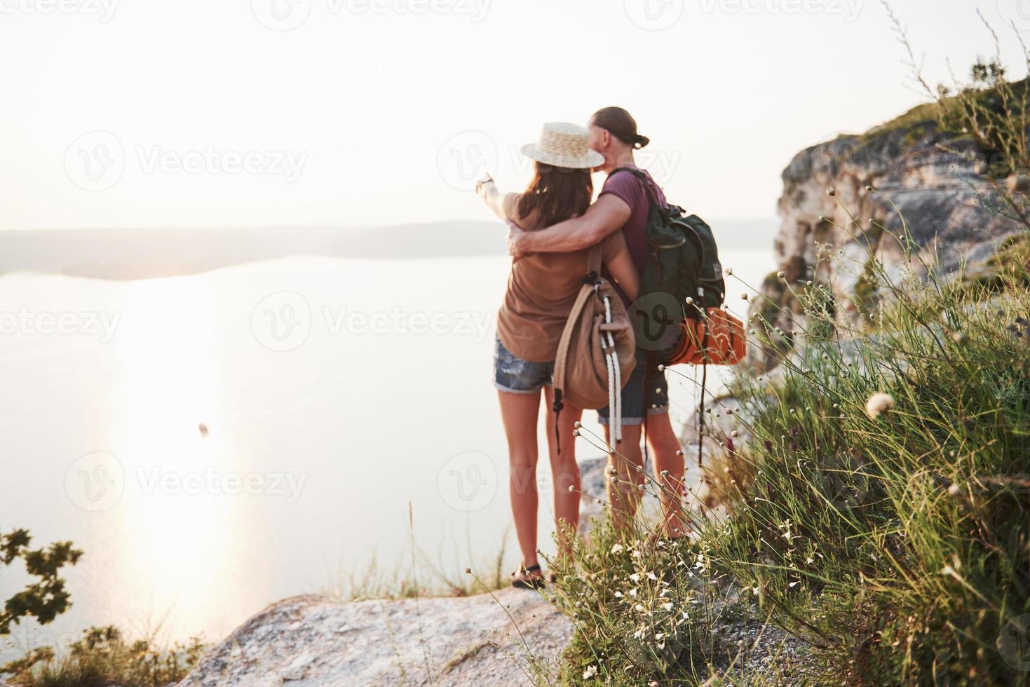 twee toeristische mannen en vrouwen met rugzakken staan naar de top van de rots en genieten van de zonsopgang. reizende bergen en kust, vrijheid en actief levensstijlconcept foto