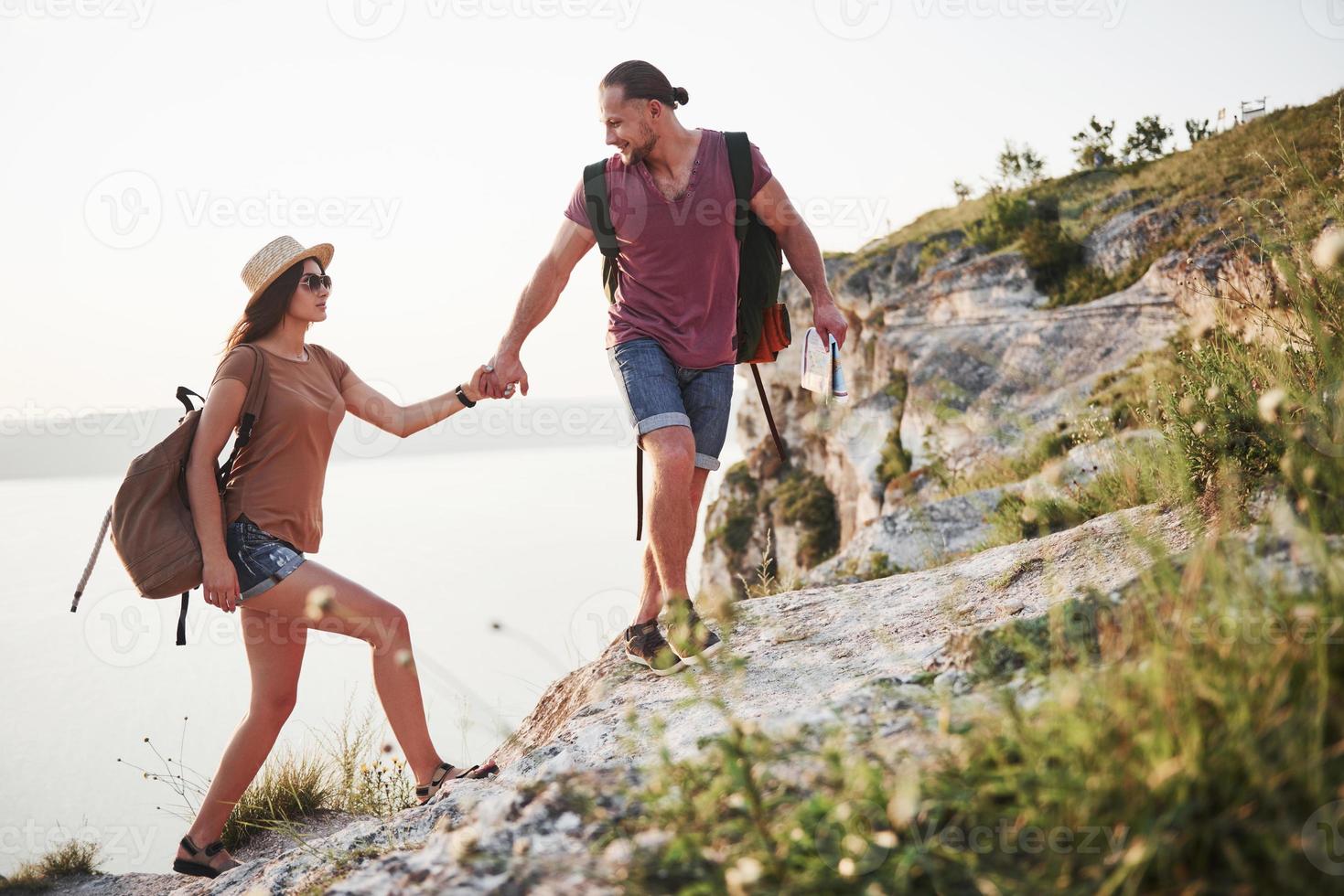 twee toeristen met rugzakken klimmen naar de top van de berg en genieten van zonsopgang foto