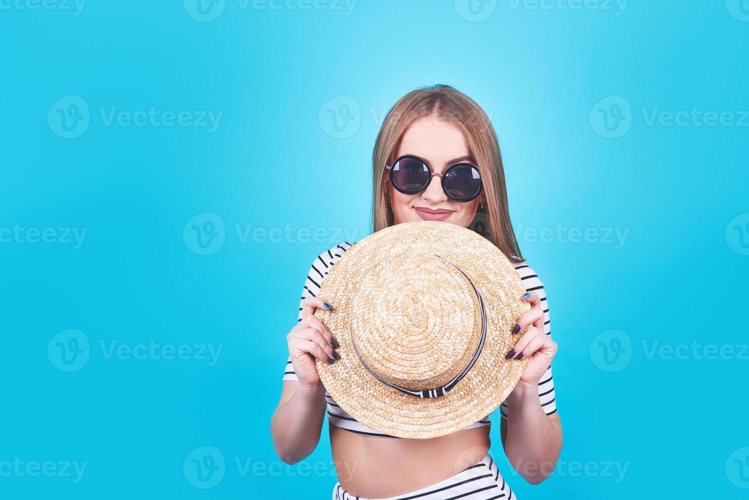 aantrekkelijk meisje in een witte en zwarte strepen, hoed, zonnebril, emotioneel geopende mond op een helderblauwe achtergrond met een perfect lichaam. geïsoleerd. studio opname foto