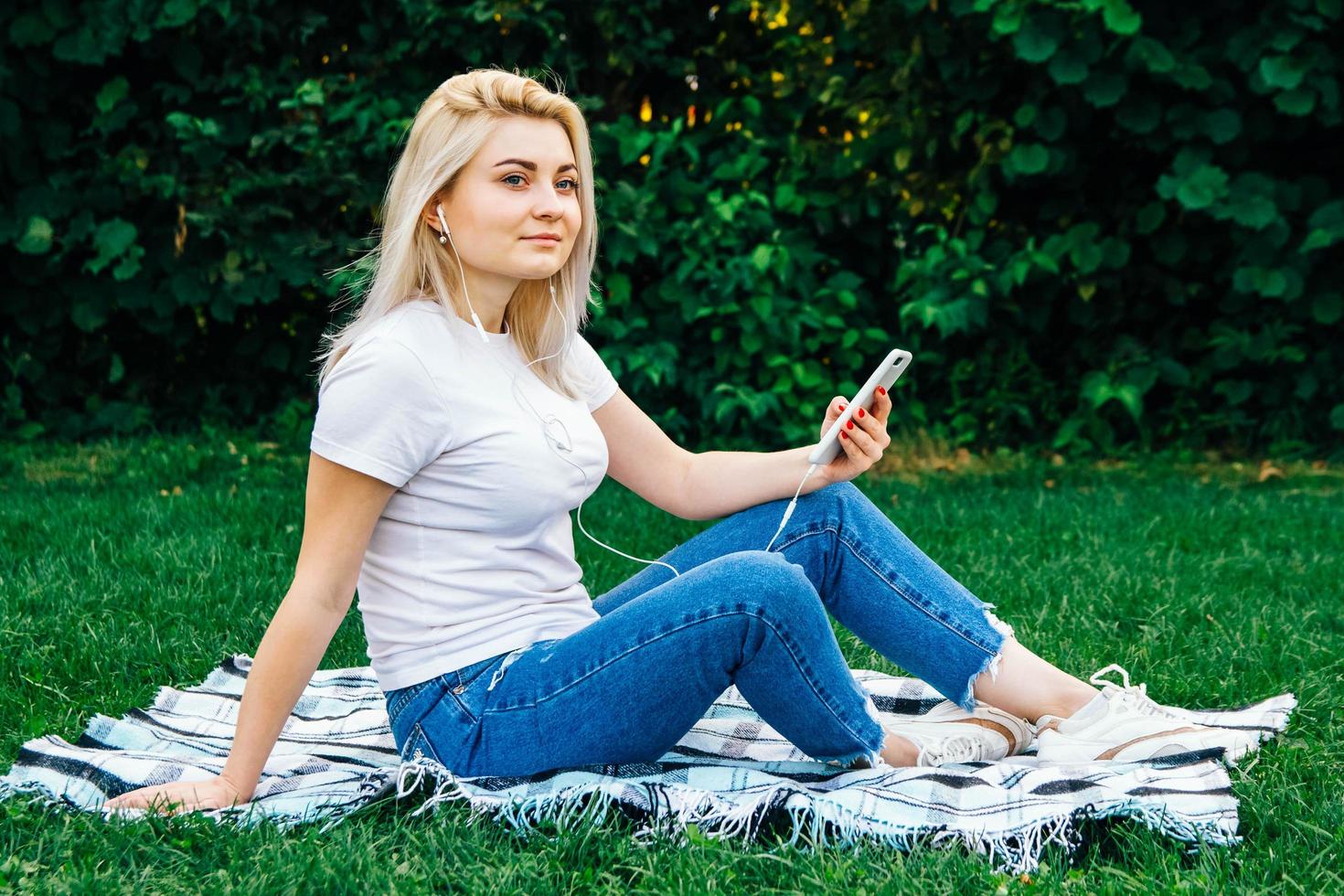 vrouw in koptelefoon en smartphone op groen gras foto