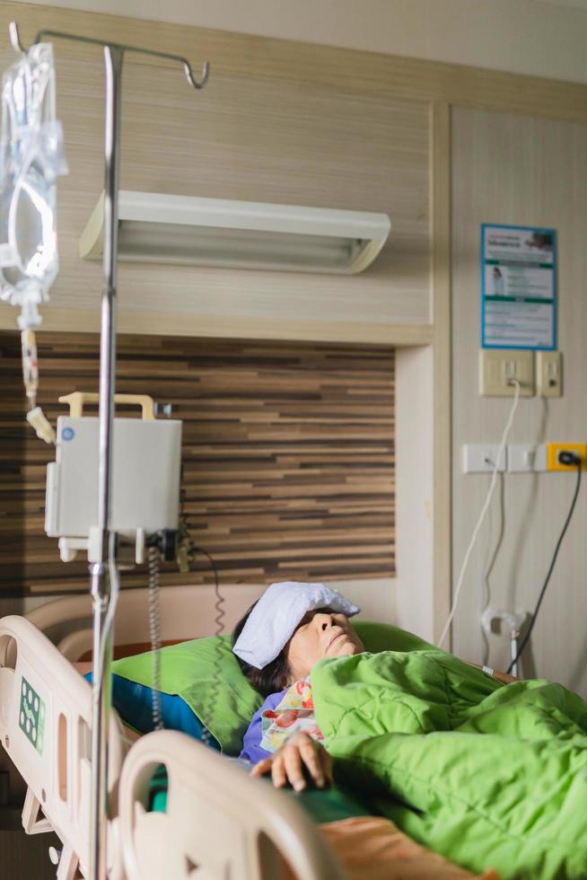 oudere vrouw patiënt liggend in bed in hpspital met kompres op voorhoofd. foto