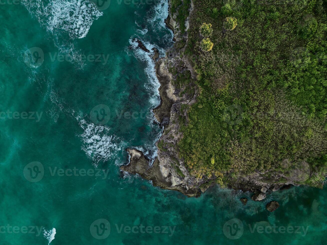 antenne. donker turkoois water met wit schuimend golven en groen rotsachtig kust foto