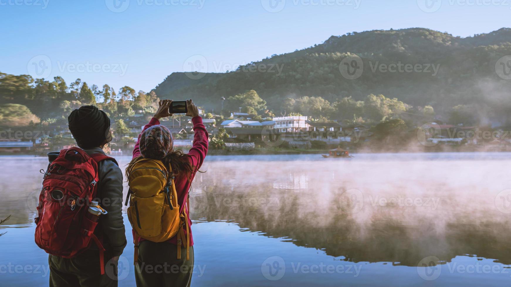 een Aziatisch stel dat 's ochtends staat te kijken naar de opkomende mist op het meer. reisverbod rak thai village, mae hong son in thailand. maak een foto van het meer