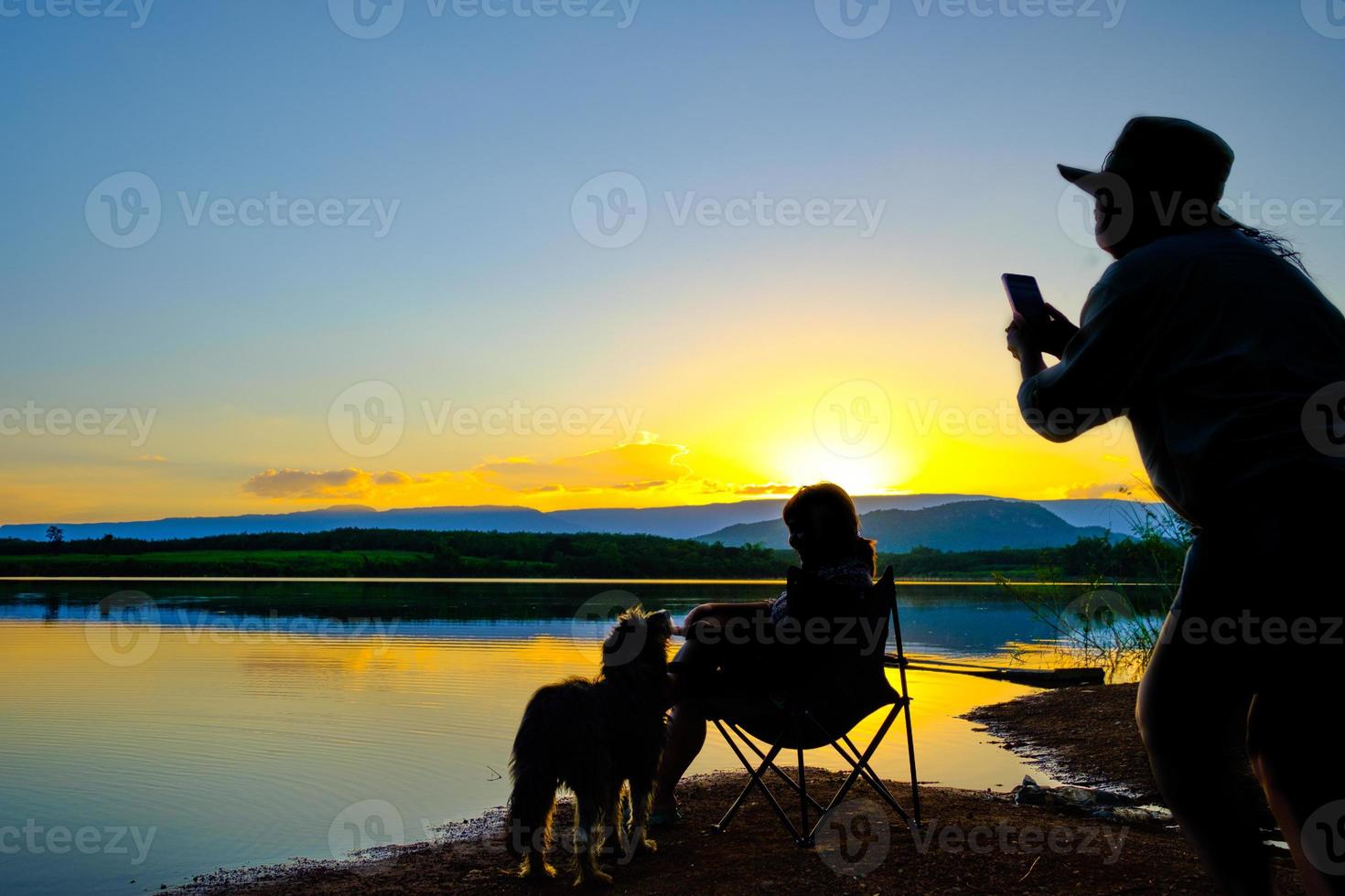 silhouetten van twee jonge vrouwen die een foto nemen over een grijze achtergrond op het meer bij zonsondergang