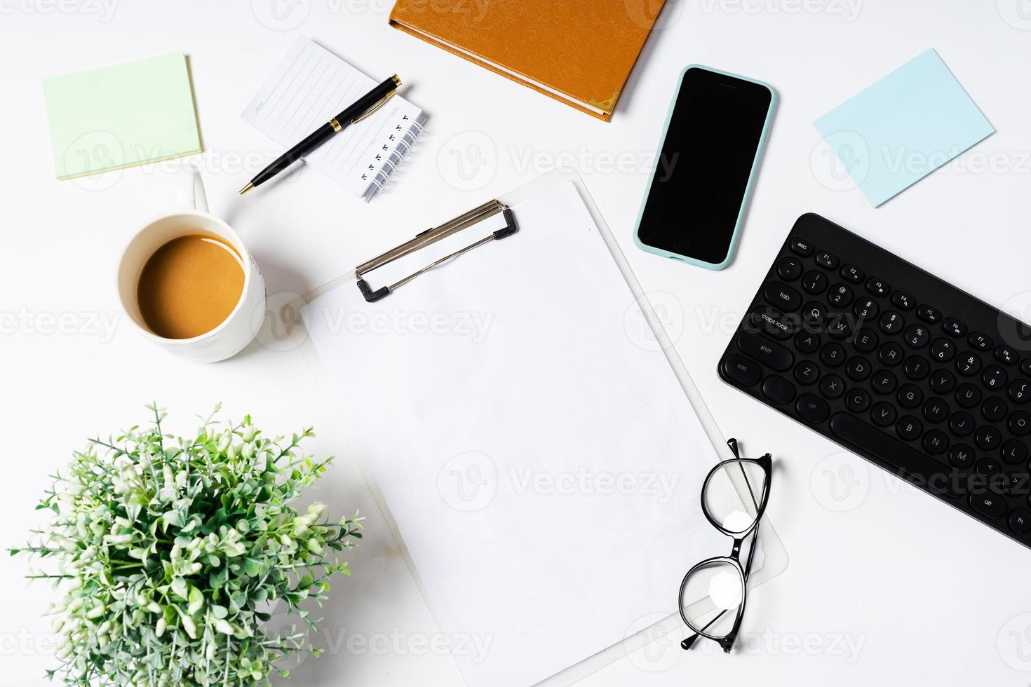bovenaanzicht van koffie, boek, notitieboekje, pen, toetsenbord, telefoon op witte achtergrond foto