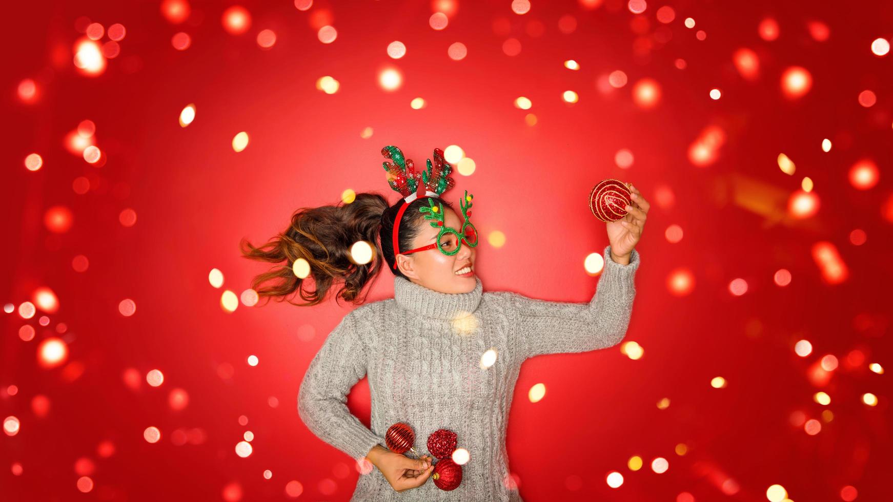 kerst nieuwjaar. jonge vrouw gekleed in warme trui met rekwisieten bal rood met kerst ornamenten in vakantie op glans rode achtergrond. concept vrolijk kerstfeest. foto