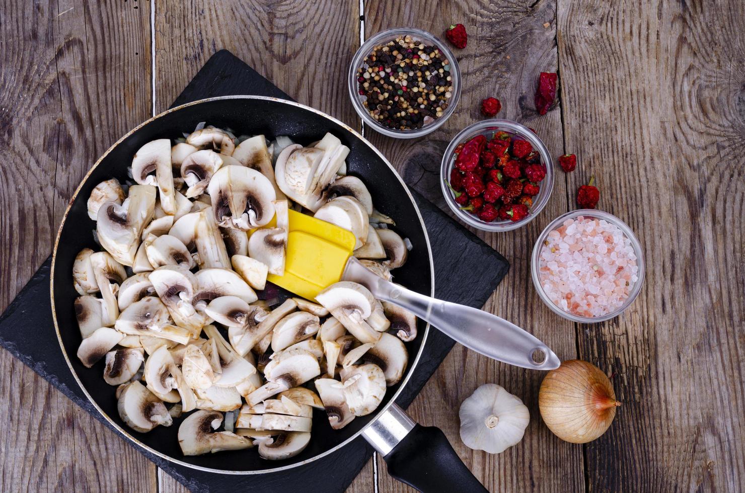 gesneden rauwe champignons in koekenpan op houten tafel. studio foto