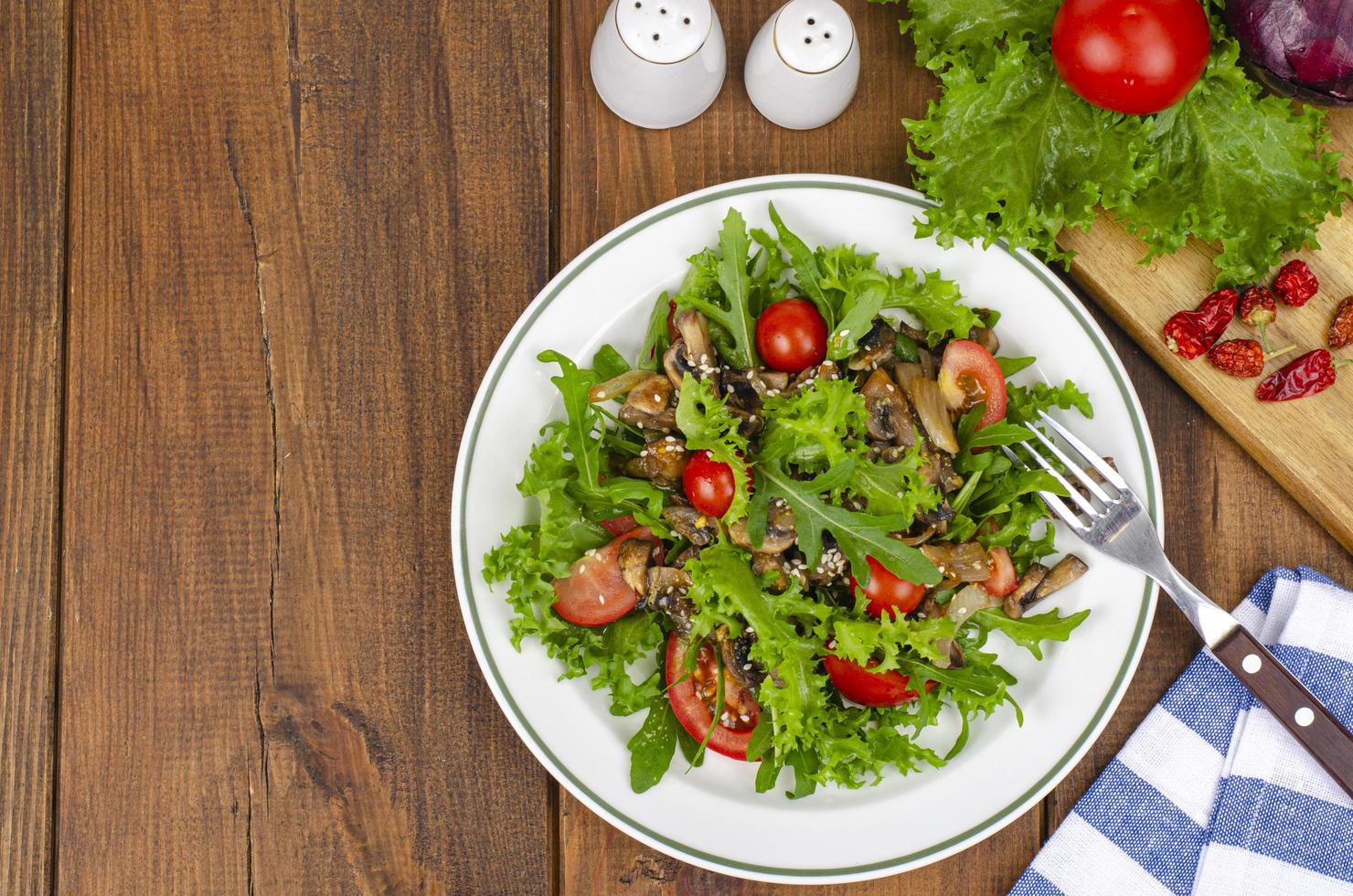 dieetsalade van rucola-bladeren, tomaten en gebakken champignons op houten tafel. studio foto