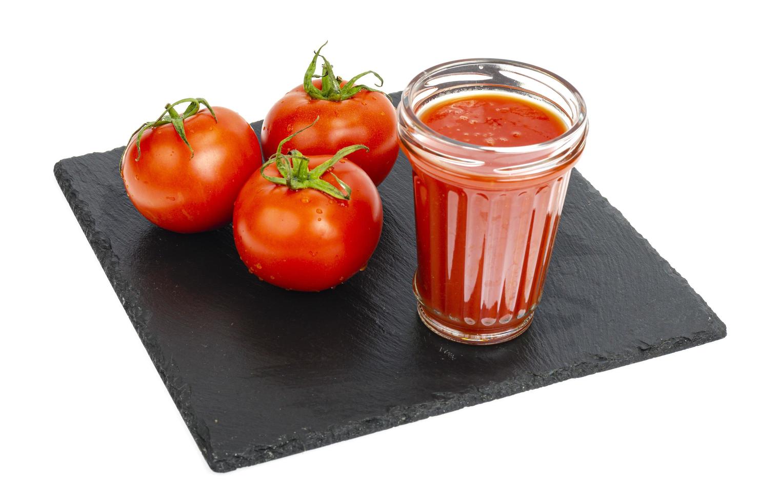 glas tomatensap, rijpe rode tomaten op zwart stenen dienblad foto