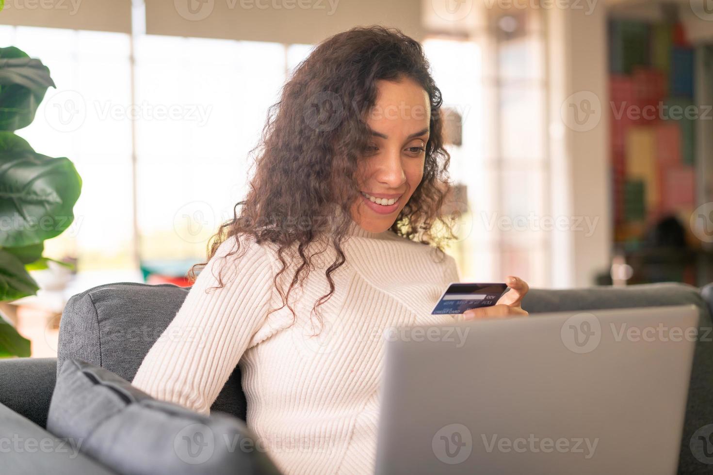 Latijnse vrouw die laptop en hand met creditcard gebruikt om op de bank te winkelen foto