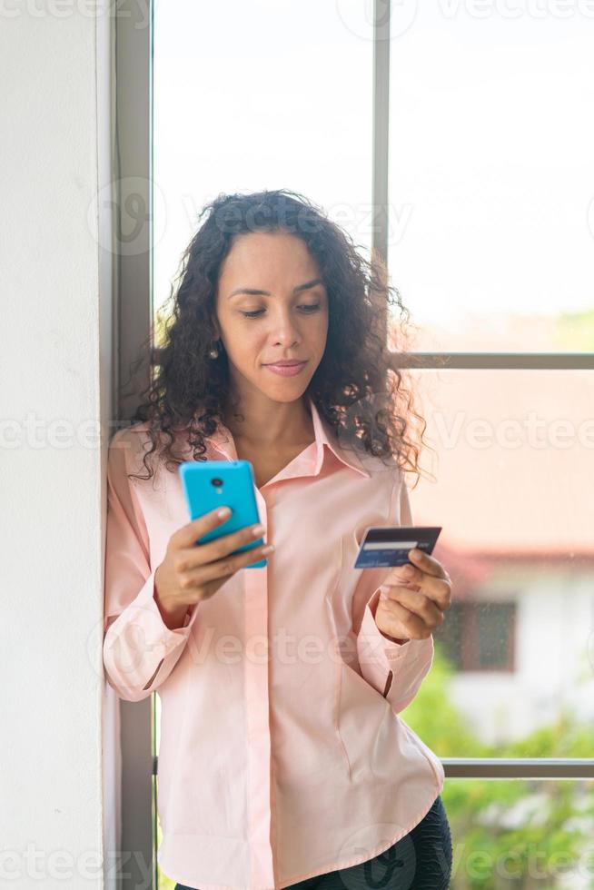 mooie latijnse vrouw die smartphone met creditcard gebruikt foto