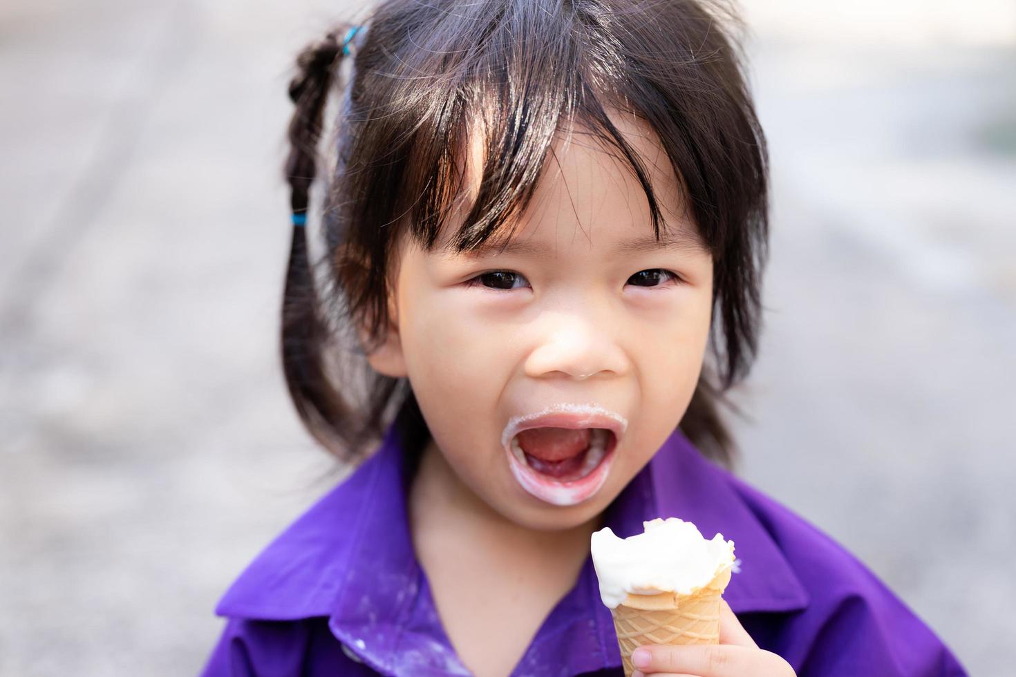 klein meisje dat witte roomijskegel eet. kind verknalde haar mond als toetje. kinderen glimlachen blij. warm weer met dessert en koud. foto