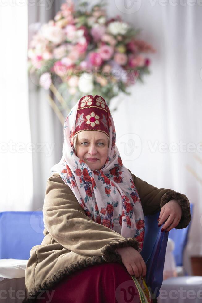 een mooi ouderen Russisch vrouw dame in de nationaal hoofdtooi kokoshnik en schapenvacht jas glimlacht en looks Bij de camera. foto
