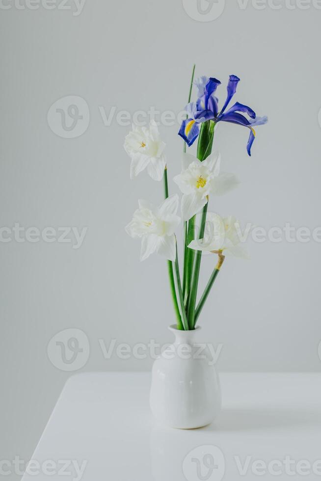 boeket van inschrijving gele narcis narcis en iris bloemen in een vaas Aan een wit tafel . foto