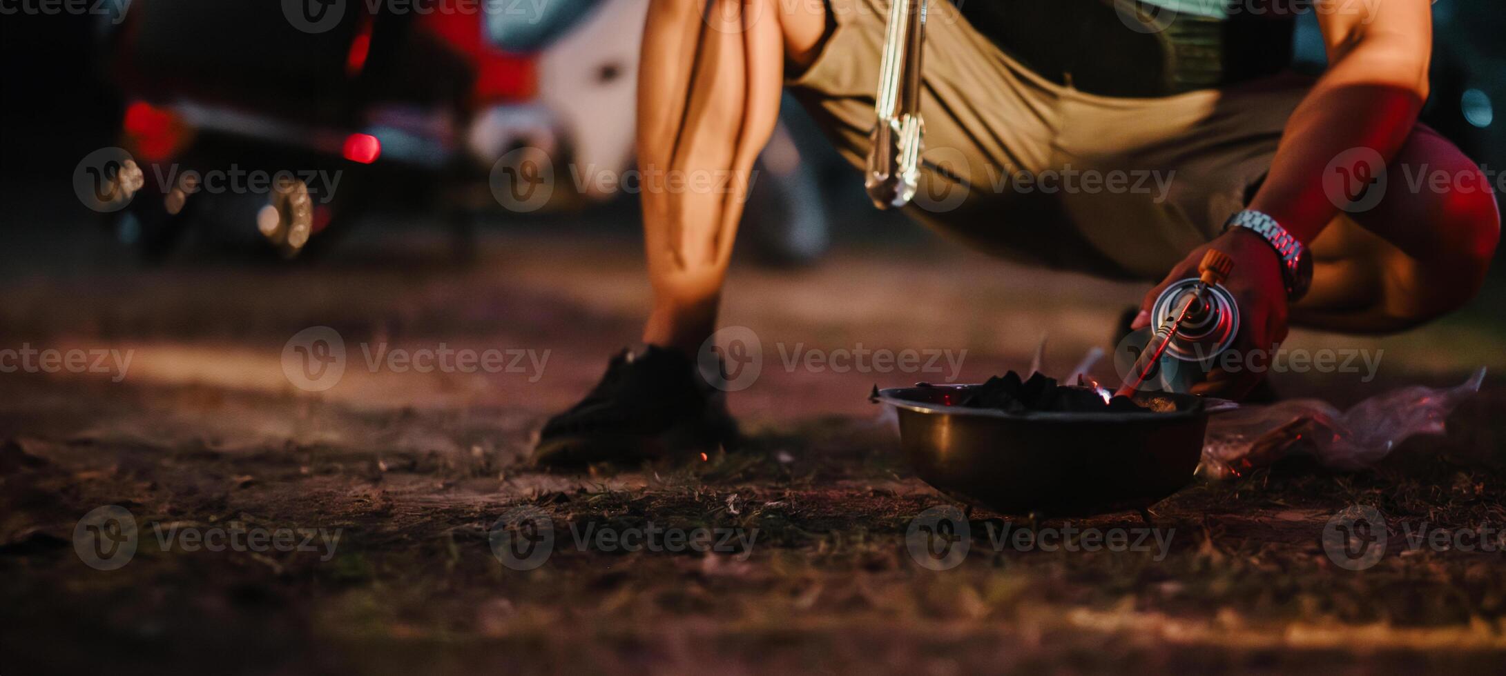 camper hurkt naar licht een houtskool rooster Bij schemering, met een rood gloed verhelderend de camping atmosfeer. foto