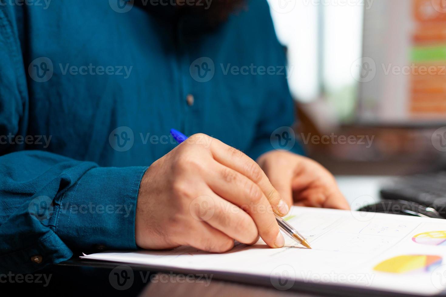 close-up van de hand van de ondernemer die aan tafel zit en document met bedrijfsplan analyseert foto