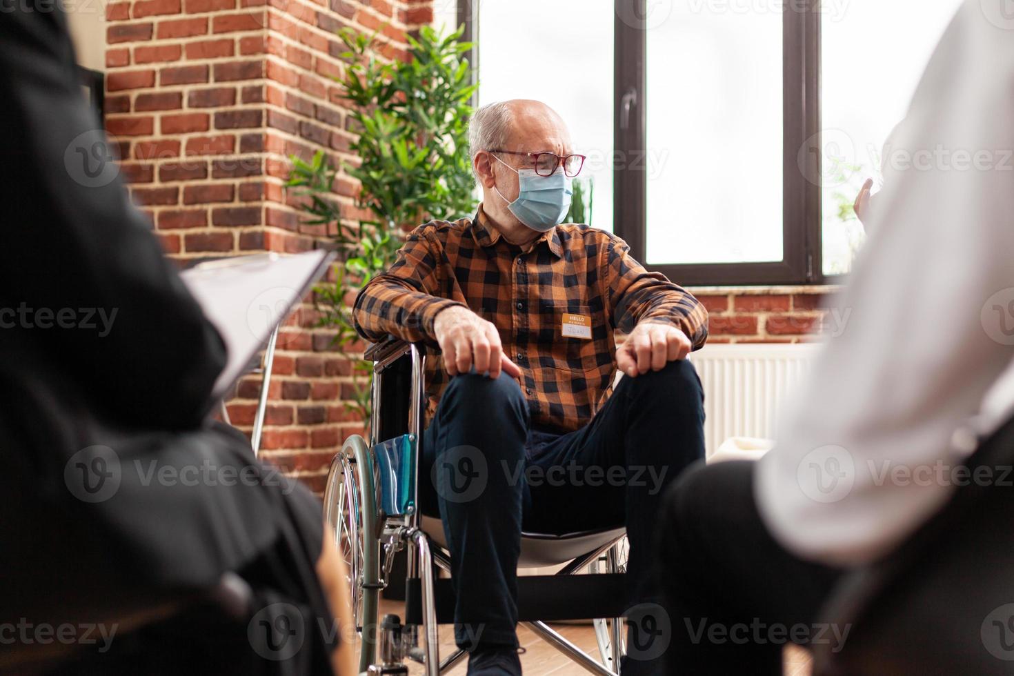 senior persoon met een handicap die groepstherapiesessie bijwoont, gezichtsmasker draagt foto