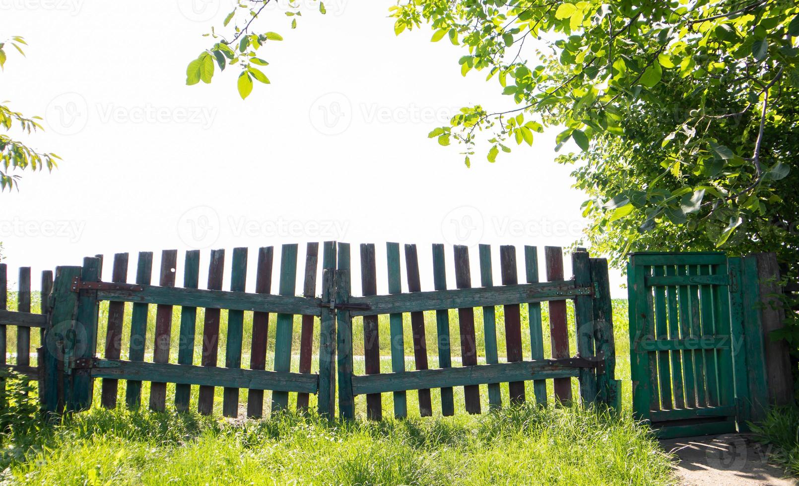 schilderachtig uitzicht op de oude houten poort met bomen in de tuin en een groen gazon op een zonnige zomerdag. foto