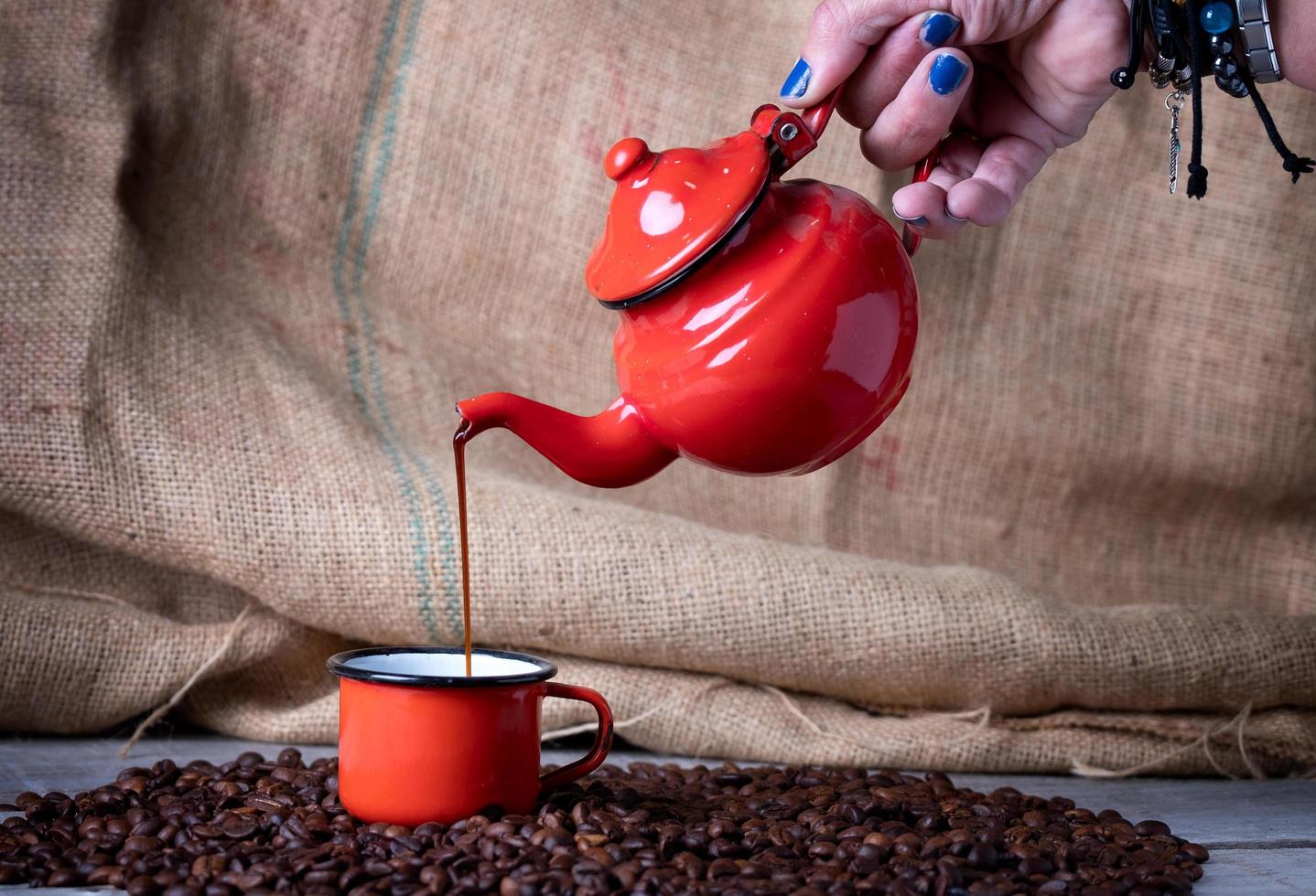 hand met blauwe nagels met rode metalen theepot die koffie maakt in een rode metalen beker foto