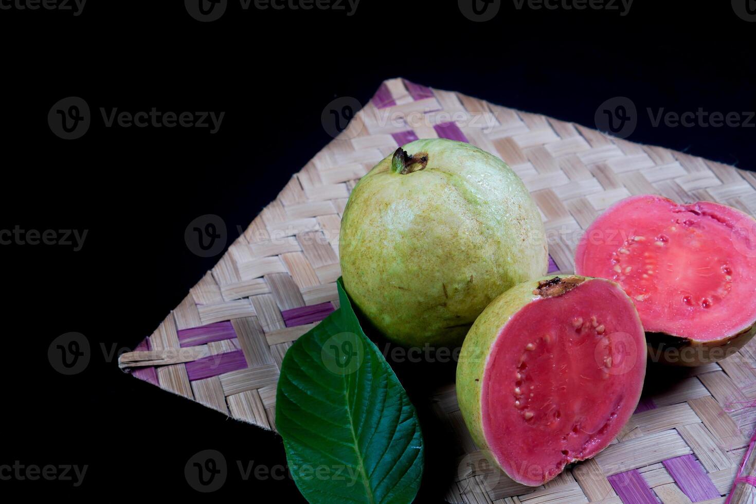 guava geïsoleerd. verzameling van rood vleesgeworden guava fruit met geelachtig groen huid en bladeren geïsoleerd Aan zwart achtergrond met geweven bamboe. foto