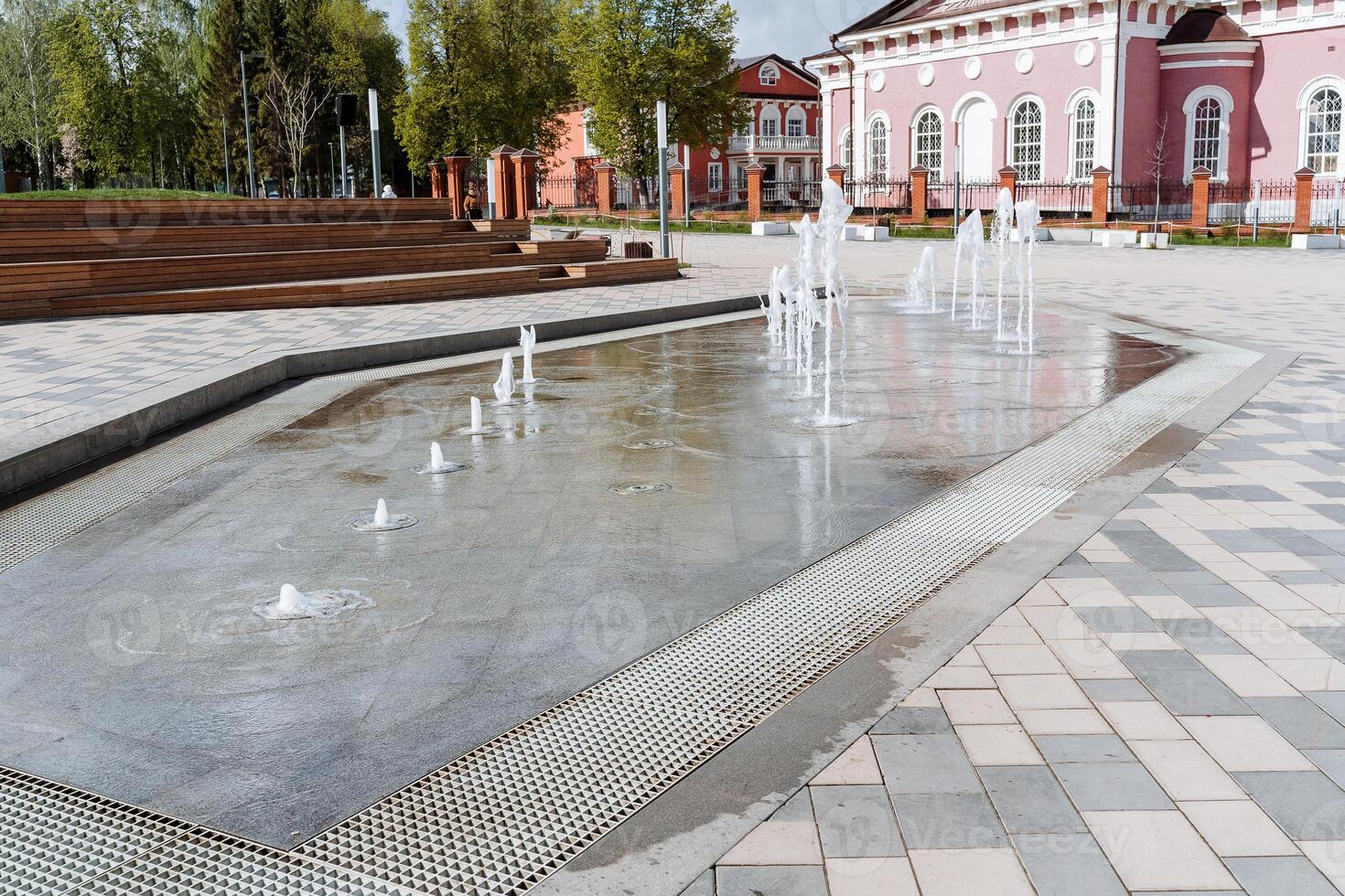 een fontein in de stad- vierkant, stralen van water stijgende lijn van hieronder van onder de stoep, een onderhoudend fontein voor kinderen, dansen spatten van water Aan een zomer dag. foto