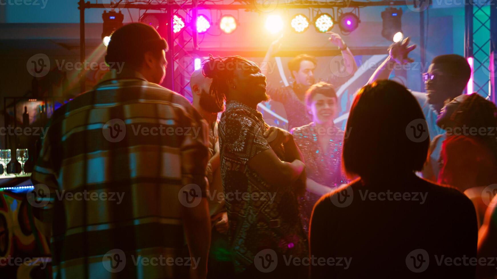 gelukkig vrienden dansen Aan funky muziek, feesten samen met dj Aan stadium en schijnwerpers. groep van verschillend mensen jumping in de omgeving van Aan dans verdieping en hebben pret Bij naar een discotheek gaan evenement. handheld schot. foto