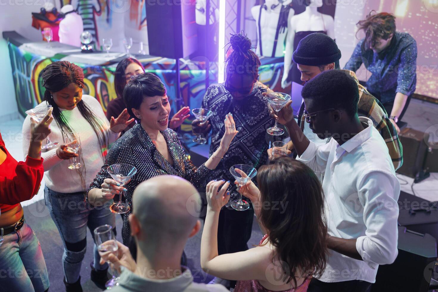 vrienden drinken alcohol terwijl dansen en het zingen Bij nachtclub feest. zorgeloos jong mensen genieten van dranken, Holding bril en gezegde geroosterd brood terwijl naar een discotheek gaan Aan dansvloer foto