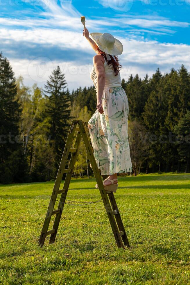 een vrouw Aan een houten ladder verven de blauw lucht foto