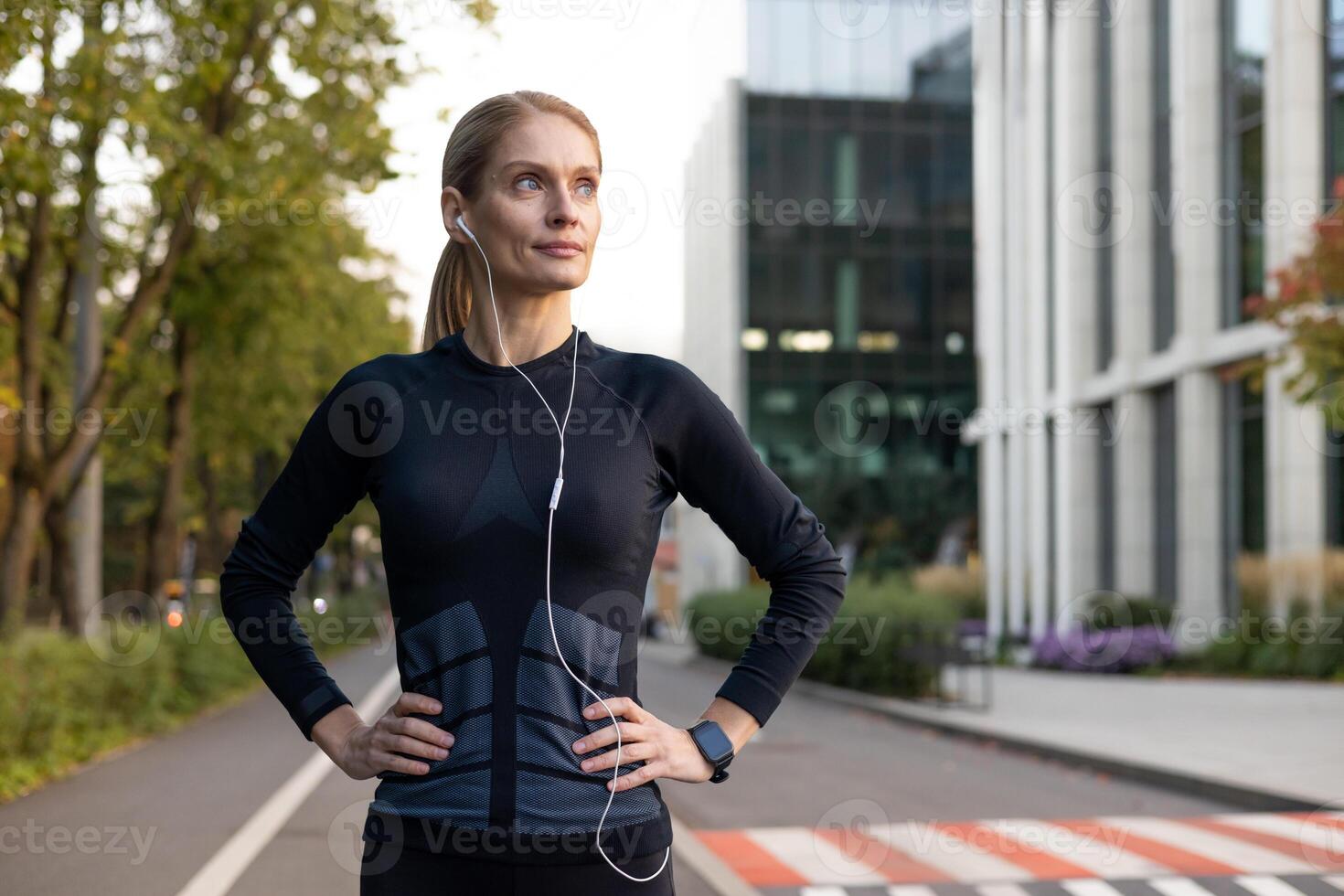 een fitness gericht vrouw pauzeert gedurende haar rennen in de stad, weergeven bepaling en vertrouwen. vervelend sportkleding en oortelefoons, ze belichaamt een actief levensstijl tegen een stedelijk achtergrond. foto