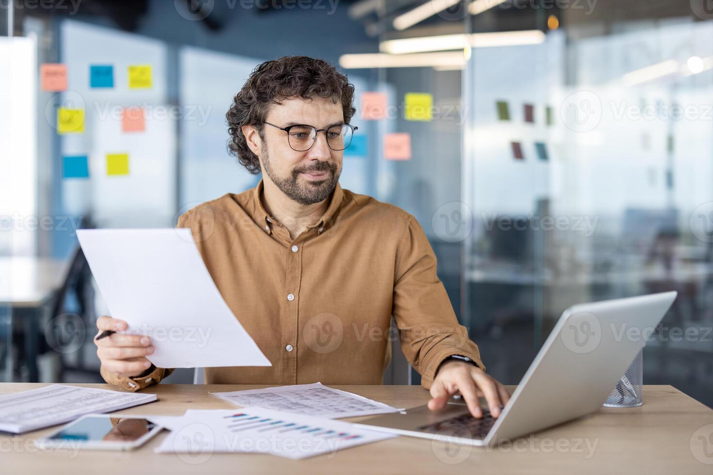 een gefocust mannetje bedrijf professioneel beoordelingen belangrijk documenten Bij zijn bureau in een hedendaags kantoor instelling, illustreren toewijding en concentratie. foto