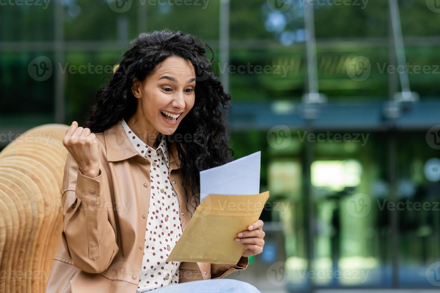 blij vrouw zittend buiten, vuist pompen terwijl lezing uitstekend nieuws in een brief, uitdrukken opwinding en geluk. foto
