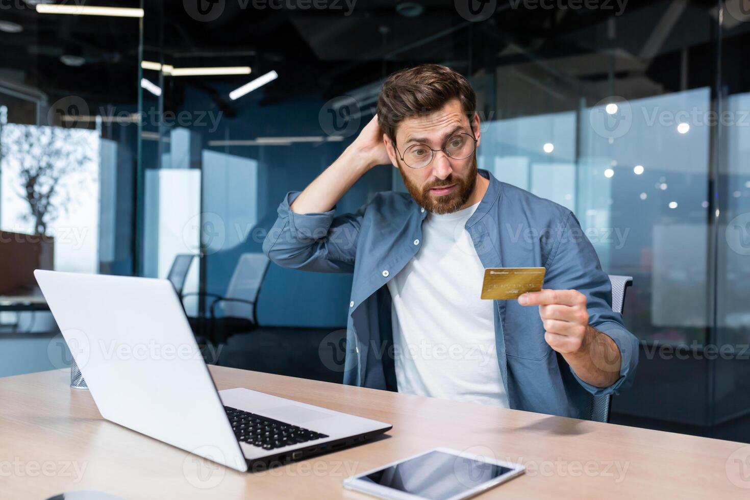 gefrustreerd en bedrogen zakenman in kantoor proberen naar maken aankoop in online op te slaan en online geld overdracht van bank credit kaart, geërgerd Mens werken binnen kantoor gebruik makend van laptop en telefoon. foto