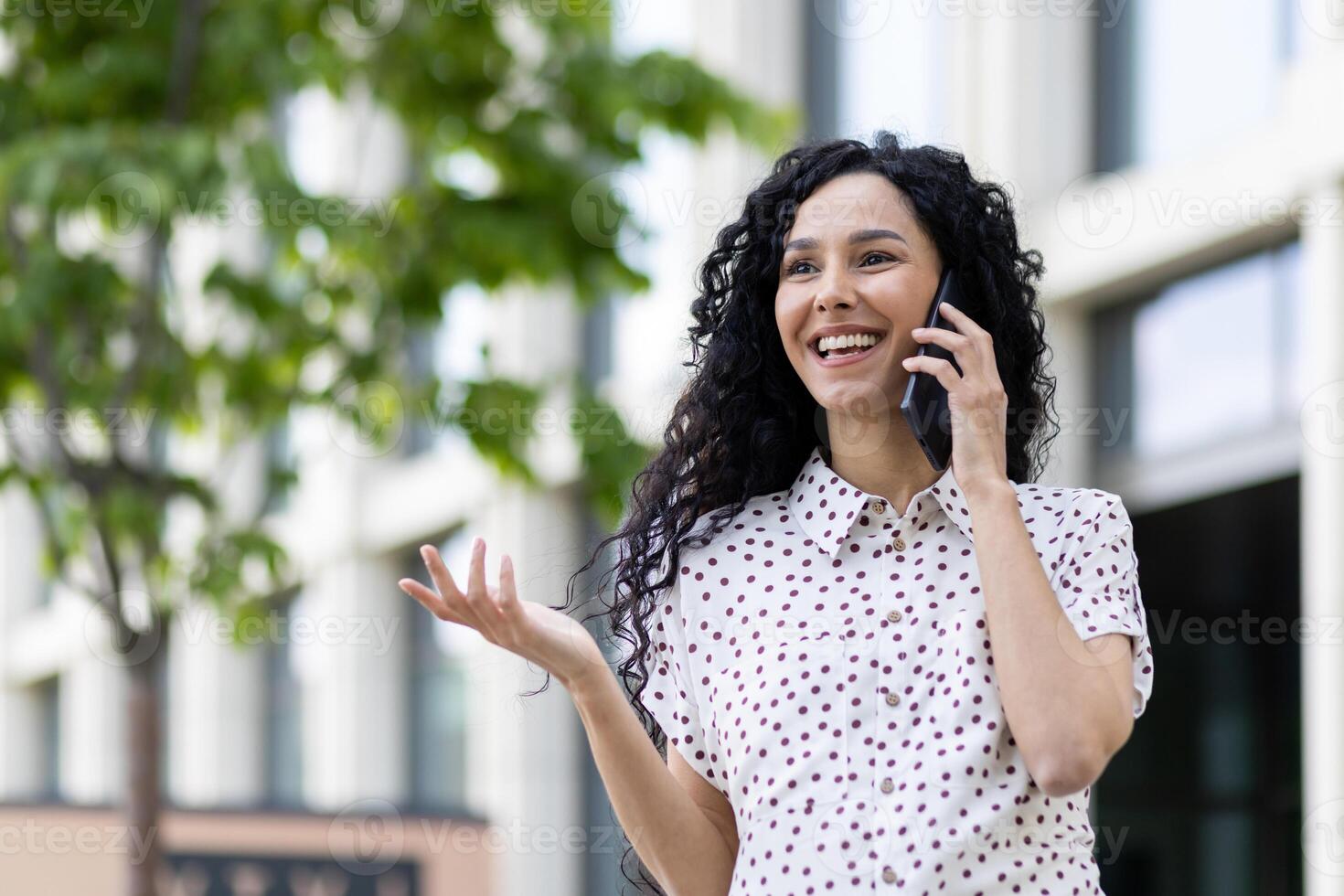 jong mooi vrouw pratend Aan de telefoon detailopname terwijl wandelen in de stad, bedrijf vrouw glimlachen tevreden, geslaagd Latijns Amerikaans vrouw met gekruld haar- Aan een zonnig dag. foto