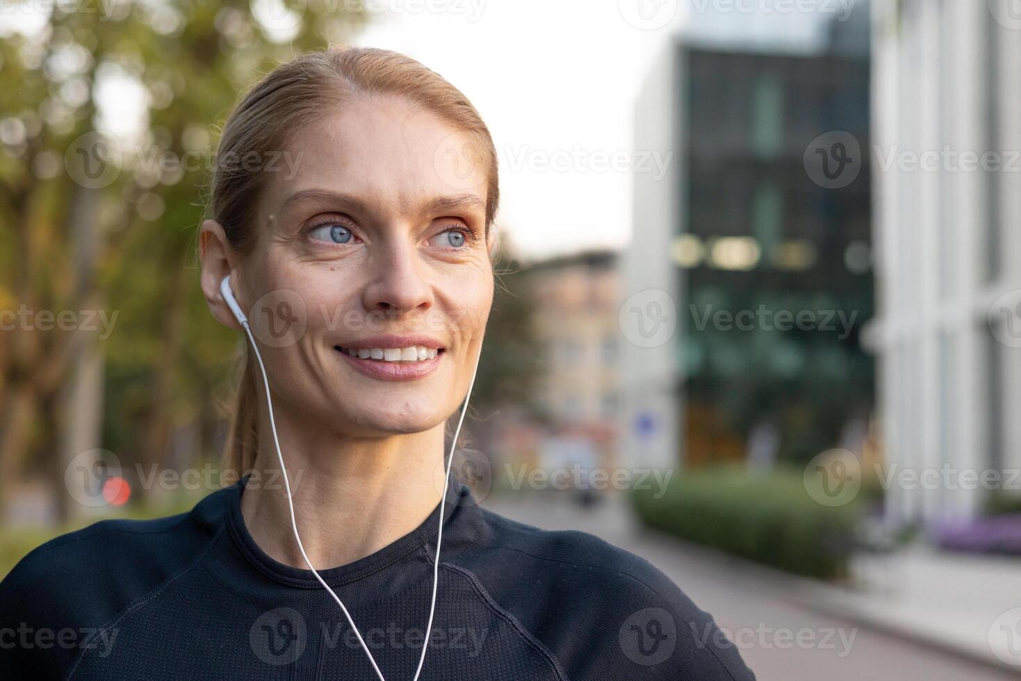 fit vrouw jogger met oortelefoons glimlacht terwijl oefenen in stedelijk instelling, vastleggen een moment van vreugde en welzijn. foto
