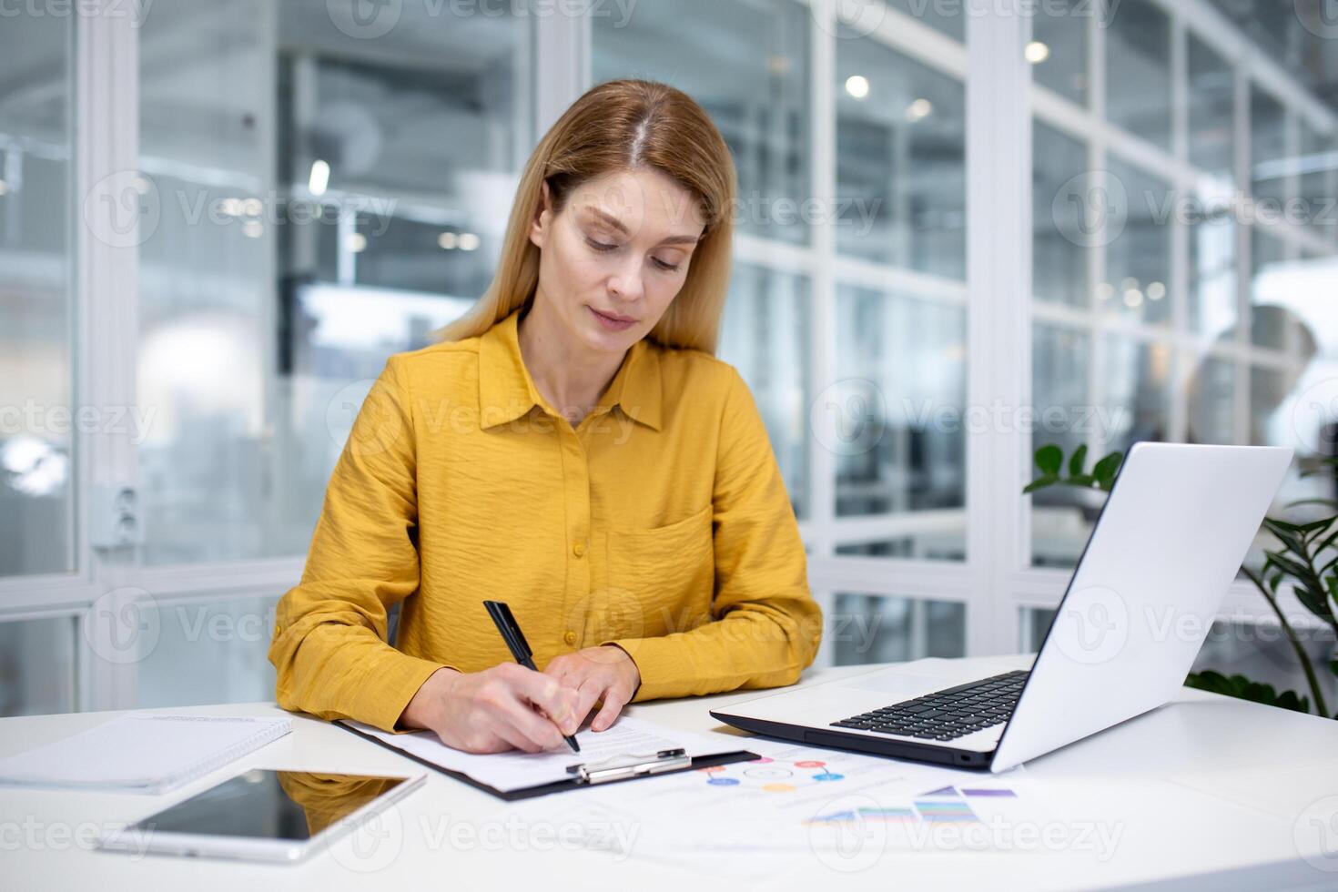 echt denken bedrijf vrouw achter papier werk, vrouw baas geconcentreerd schrijven documenten werken met papieren grafieken en grafieken binnen kantoor Bij werkplaats gebruik makend van rekenmachine en laptop. foto