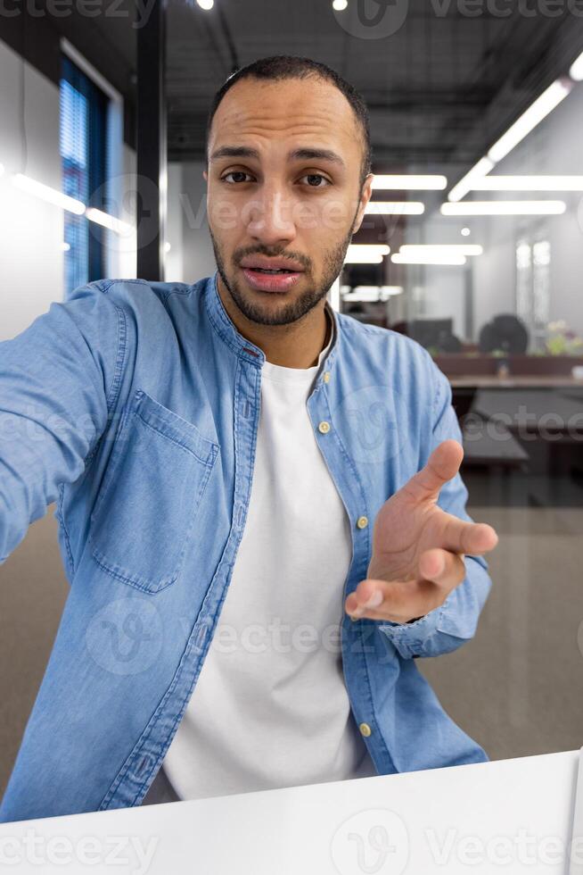 een Mens in een blauw overhemd is op zoek Bij de camera en richten zijn hand. hij is in een professioneel instelling, mogelijk Bij werk foto