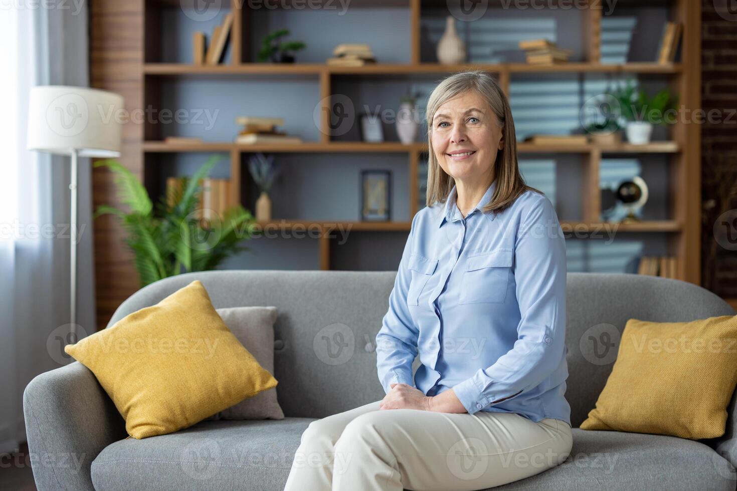 portret van een ontspannen volwassen vrouw glimlachen en zittend comfortabel Aan een bankstel met elegant interieur achtergrond. foto