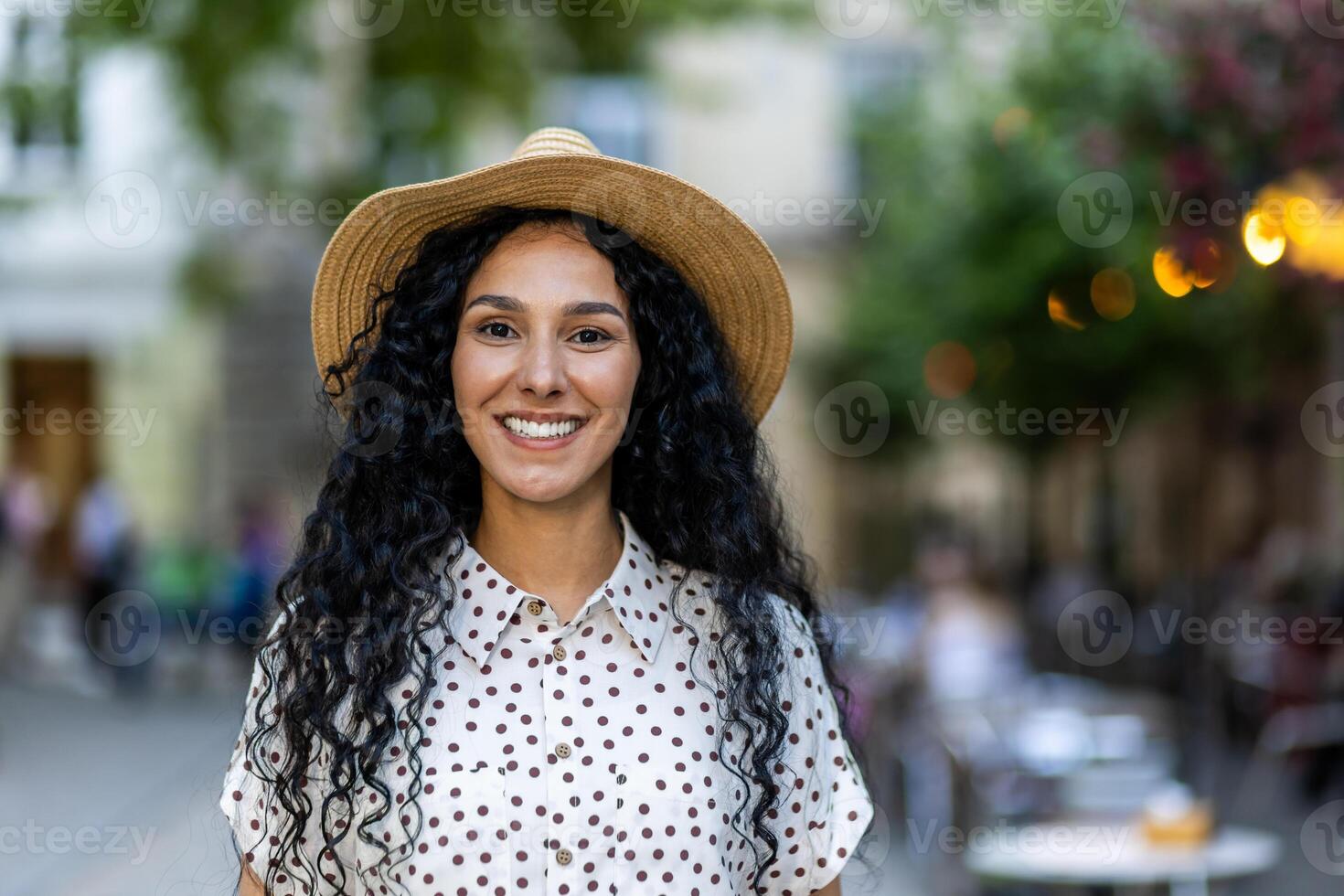 mooi jong Latijns Amerikaans vrouw portret, vrouw wandelen in avond stad in hoed met gekruld haar- in warm het weer, glimlachen en op zoek Bij camera dichtbij omhoog. foto