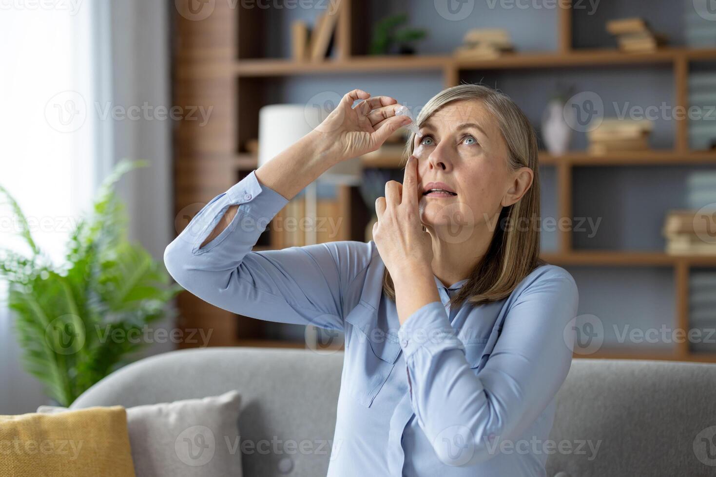 geconcentreerd volwassen dame fooien hoofd terug en vaststelling positie voor toepassen medisch oog druppels binnenshuis. ongezond vrouw met oogheelkunde problemen gebruik makend van hydraterend behandeling voor visie zorg. foto