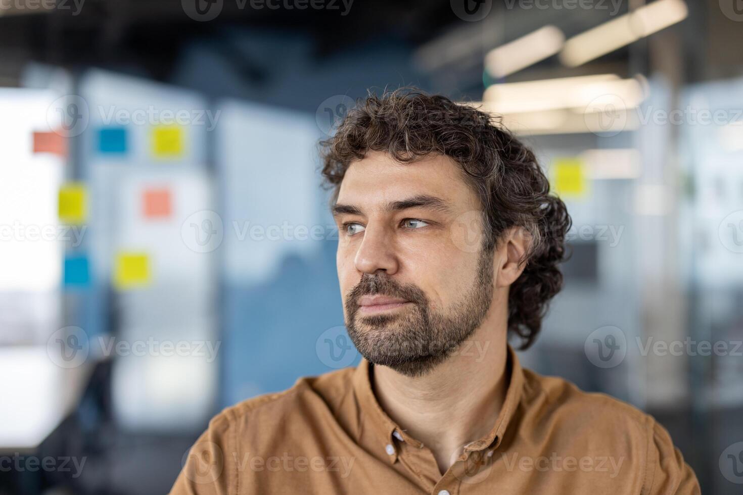 een professioneel mannetje in gewoontjes bedrijf kleding werken in een hedendaags kantoor instelling met kleurrijk kleverig aantekeningen in de achtergrond. foto