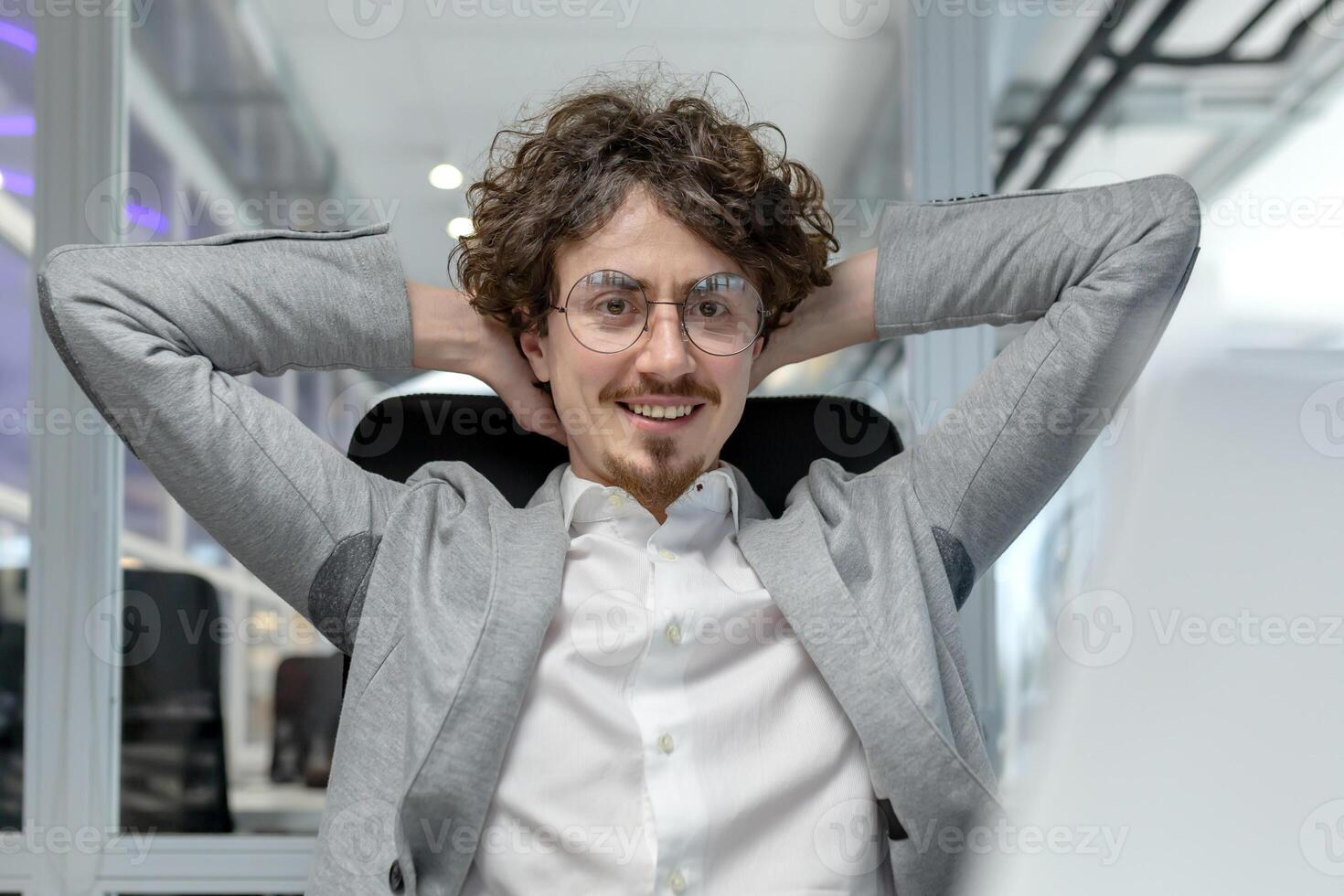 glimlachen jong volwassen zakenman tot rust komen in een kantoor stoel weergeven bevoegdheid, tevredenheid, en tevredenheid na bekwaam werk prestatie. foto