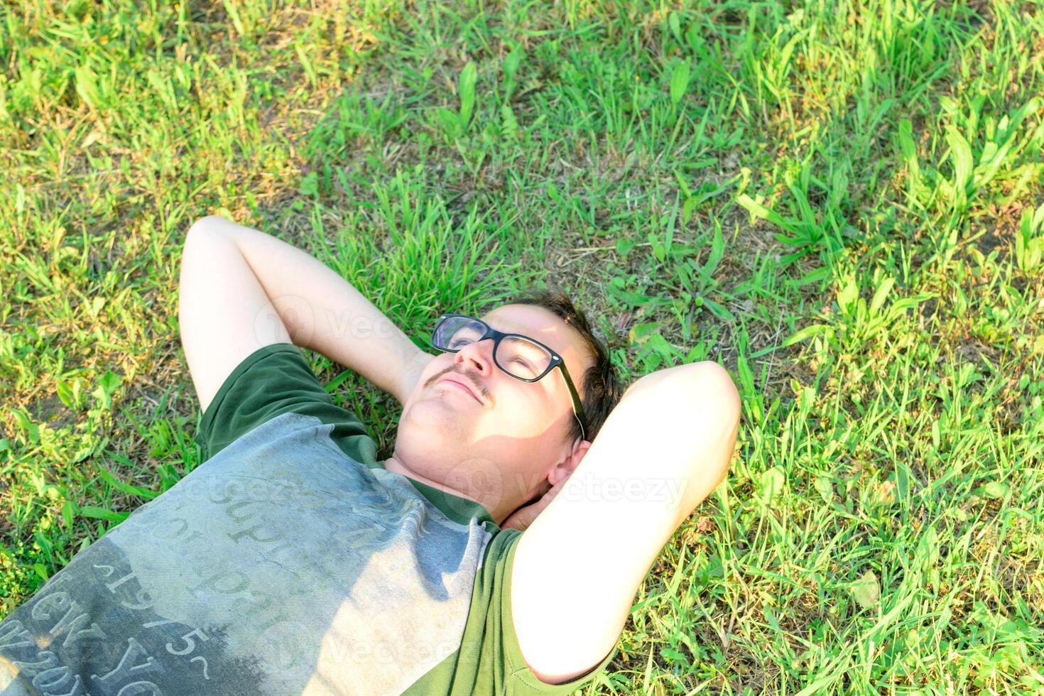 jong Mens met bril gelogen Aan gras genieten van vakantie na aan het studeren heel gelukkig foto