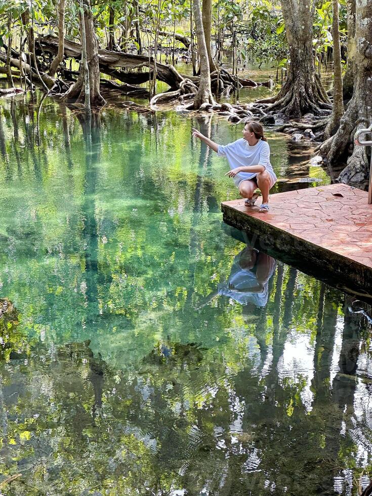 een vrouw Aan een steen platform, omringd door de weelderig groen van een tropisch Woud en de Doorzichtig wateren van een sereen vijver, reflecterend een moment van kalmte en verbinding met natuur foto